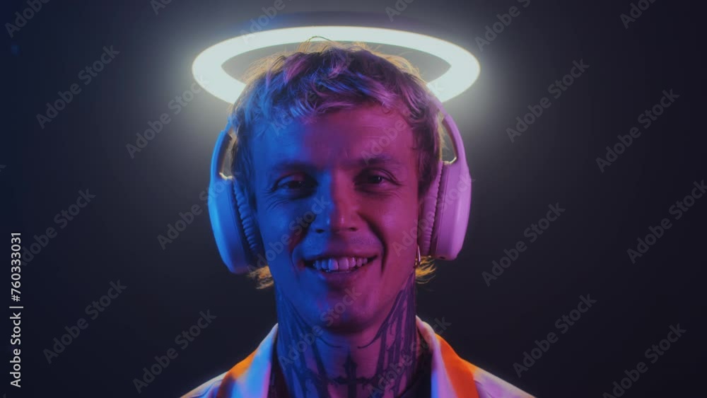 Close up portrait of young Caucasian guy in headphones smiling at camera under ring light in neon Close up portrait of young Caucasian guy in headphones smiling at camera under ring light in neon