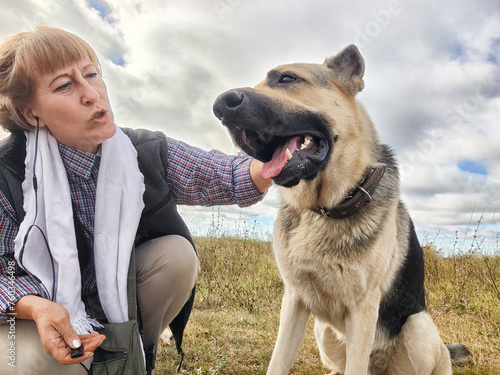 Adult girl with shepherd dog taking selfies in a field. Middle aged woman and big shepherd dog on nature. Friendship, love, communication, fun, hugs © keleny