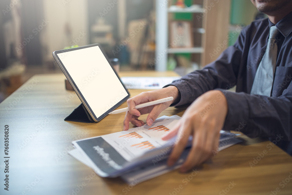 Businessman analyzing statistics on documents with a mock-up screen laptop at a workspace Businessman analyzing statistics on documents with a mock-up screen laptop at a workspace