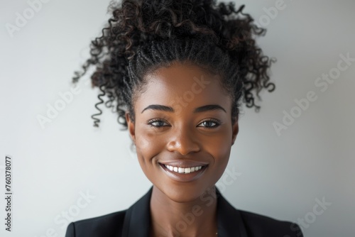 A woman with curly hair and a black jacket is smiling
