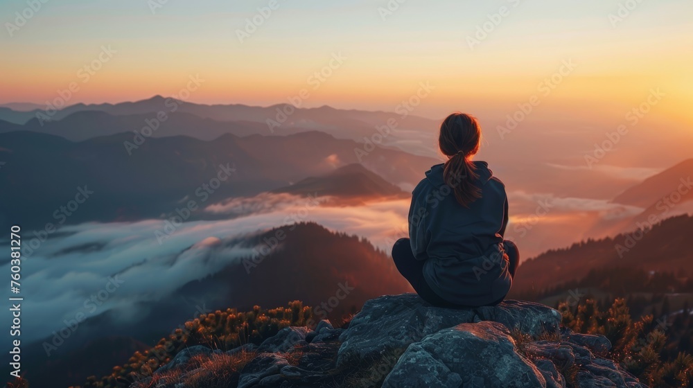 Young woman sitting on the top of a mountain and watching the misty valley.