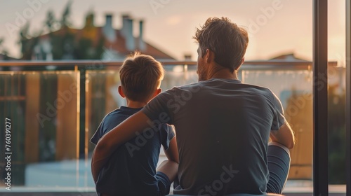 Father and son sitting on the balcony and looking at the sunset.