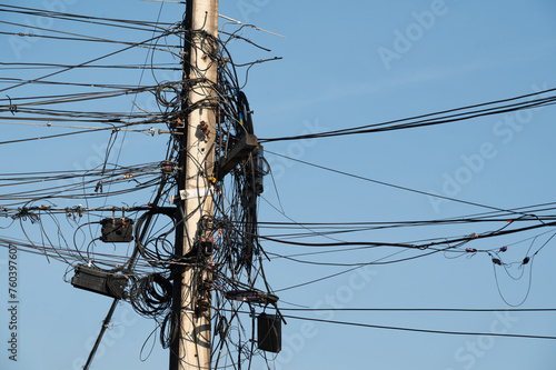 Electric post and line are on blue background.Electric post is covered by busy electric line.
