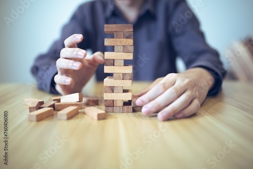 Business strategy concept with hands playing a wooden block tower game, symbolizing risk and stability. Planning risk management
