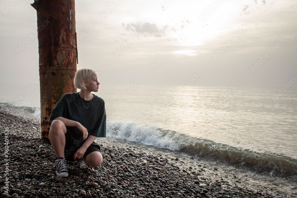 Romantic young girl with short blonde bob hair and green t-shirt dress on cold sea beach