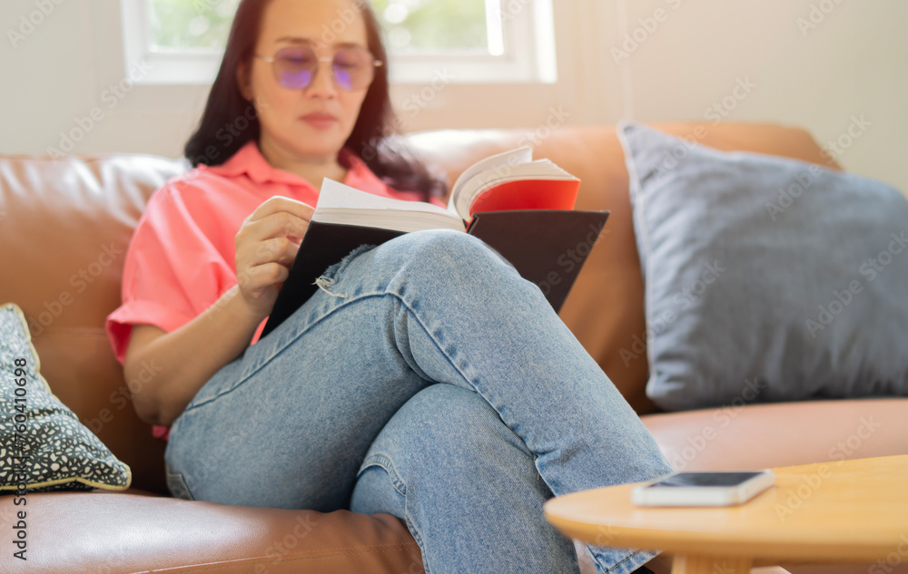 Happy adult Asian woman reading storybook on couch at home. leisure, literature and people concept. Happy adult Asian woman reading storybook on couch at home. leisure, literature and people concept.