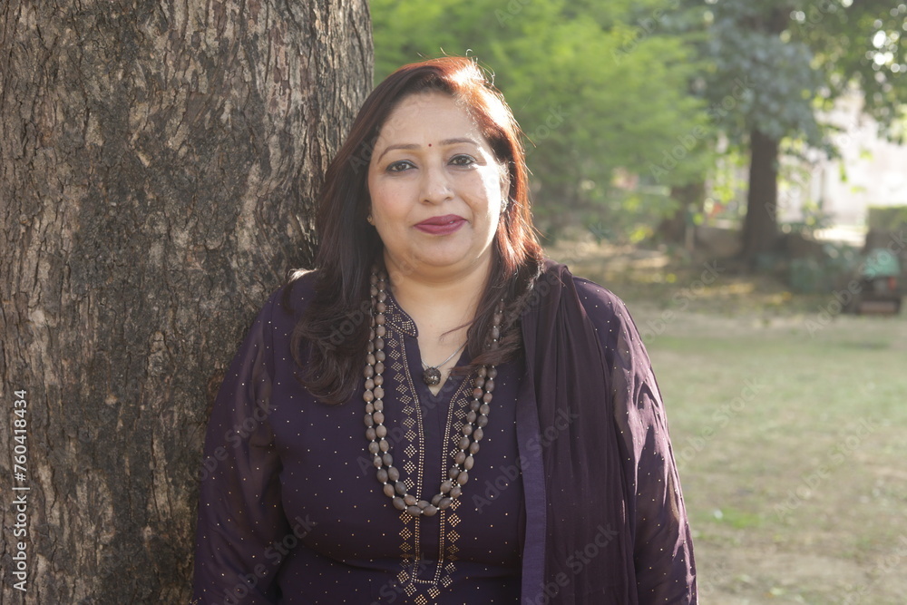 Portrait of beautiful mid aged woman standing in a lush green park. Serene and tranquil environment. lady laying on tree. pleasant weather. sunlight rim. Portrait of beautiful mid aged woman standing in a lush green park. Serene and tranquil environment. lady laying on tree. pleasant weather. sunlight rim.