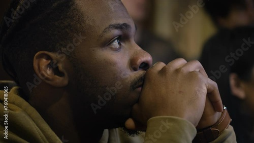 Close up of excited African American man getting upset when the team misses goal. Crowd of multiethnic sports fans or friends watch football or basketball match broadcast sitting in sports bar or pub. photo