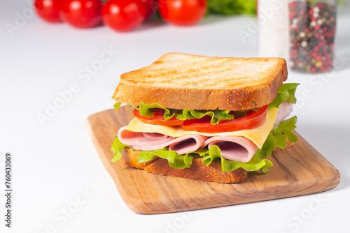 Close-up of two sandwiches with bacon, salami, prosciutto and fresh vegetables on rustic wooden cutting board. Club sandwich concept