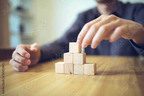 Hand strategically placing wooden blocks in a stair-step design on a table, signifying progressive success and growth