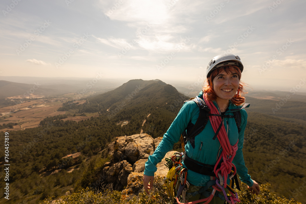 A woman in a blue jacket stands on a mountain top, smiling and looking out over the landscape A woman in a blue jacket stands on a mountain top, smiling and looking out over the landscape