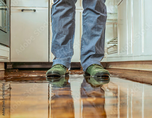 Les pieds dans l'eau, concept original pour imager un dégât des eaux, une fuite d'eau dans un appartement, vue à ras du sol des pieds du propriétaire dans une flaque d'eau 