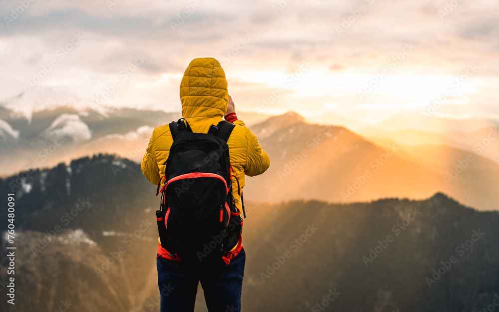 Hiker meets the beautiful sunset. Traveler hiking in mountain forest wearing cold weather accessories, wind jacket and backpack for camping outdoo - obrazy, fototapety, plakaty 