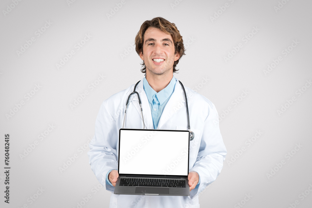 Smiling man doctor showcasing laptop with blank screen Smiling man doctor showcasing laptop with blank screen