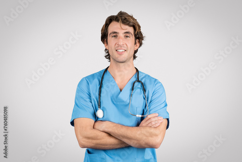 Confident male nurse in blue scrubs with arms crossed and stethoscope