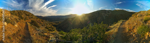 A panoramic view of a mountain range with a sun shining on the trees
