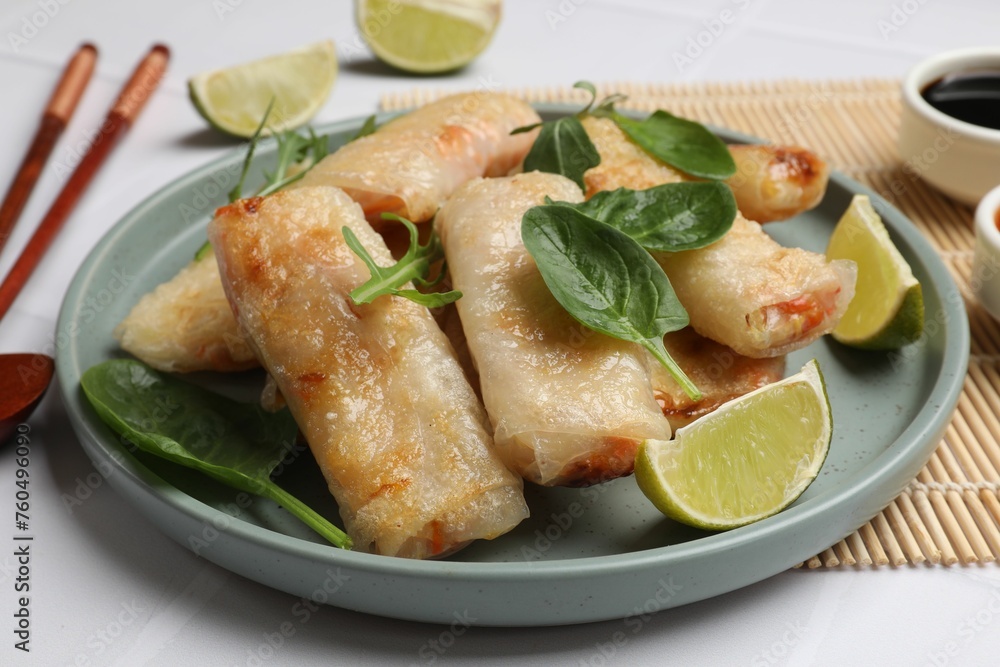 Plate with tasty fried spring rolls, spinach, arugula and lime on white table, closeup Plate with tasty fried spring rolls, spinach, arugula and lime on white table, closeup