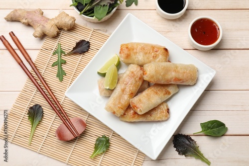 Tasty fried spring rolls, lime, sauces and other products on light wooden table, flat lay