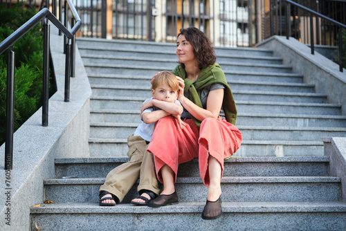 Happy family  mother and child son hugging and laugh sitting on the city stairs. motherhood concept  togetherness  love emotion. Urban city concept  residential complex in Ukraine. High quality photo