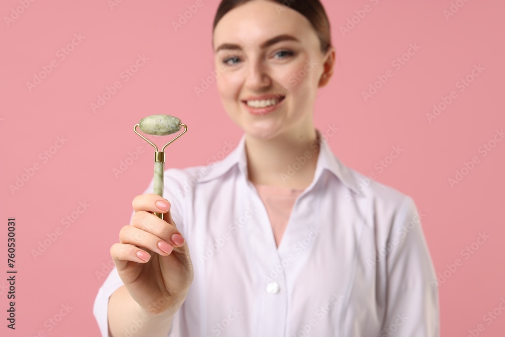 Cosmetologist with facial roller on pink background, selective focus Cosmetologist with facial roller on pink background, selective focus