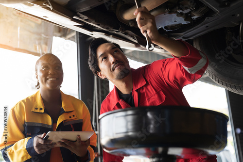 Male and female mechanic working at garage. Professional mechanics checks, repair and maintenance underneath lifted car at auto car repair service. Car service and Maintenance concept photo