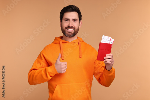 Smiling man with passport and tickets showing thumb up on beige background