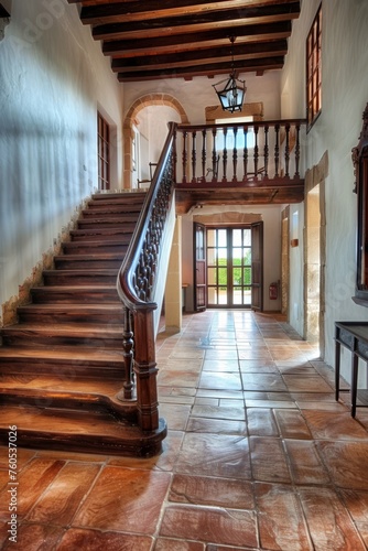 The spacious entrance hall of an old Spanish house with a wood staircase  terracotta tiles and a wooden handrail 