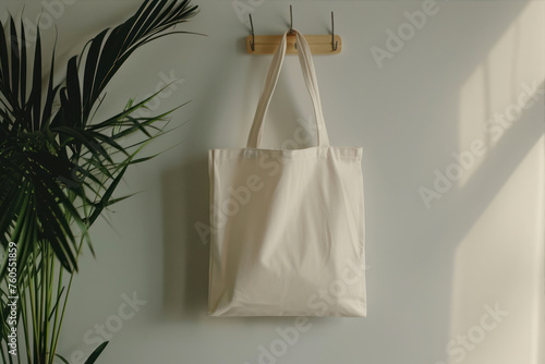 White cotton bag hanging on white wall with palm leaves. Eco friendly concept. © Ula