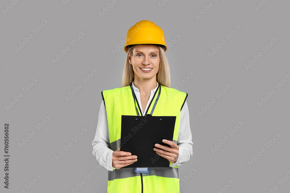 Engineer in hard hat holding clipboard on grey background Engineer in hard hat holding clipboard on grey background