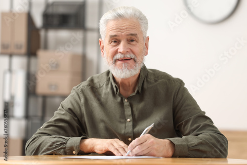 Senior man signing Last Will and Testament at table indoors photo