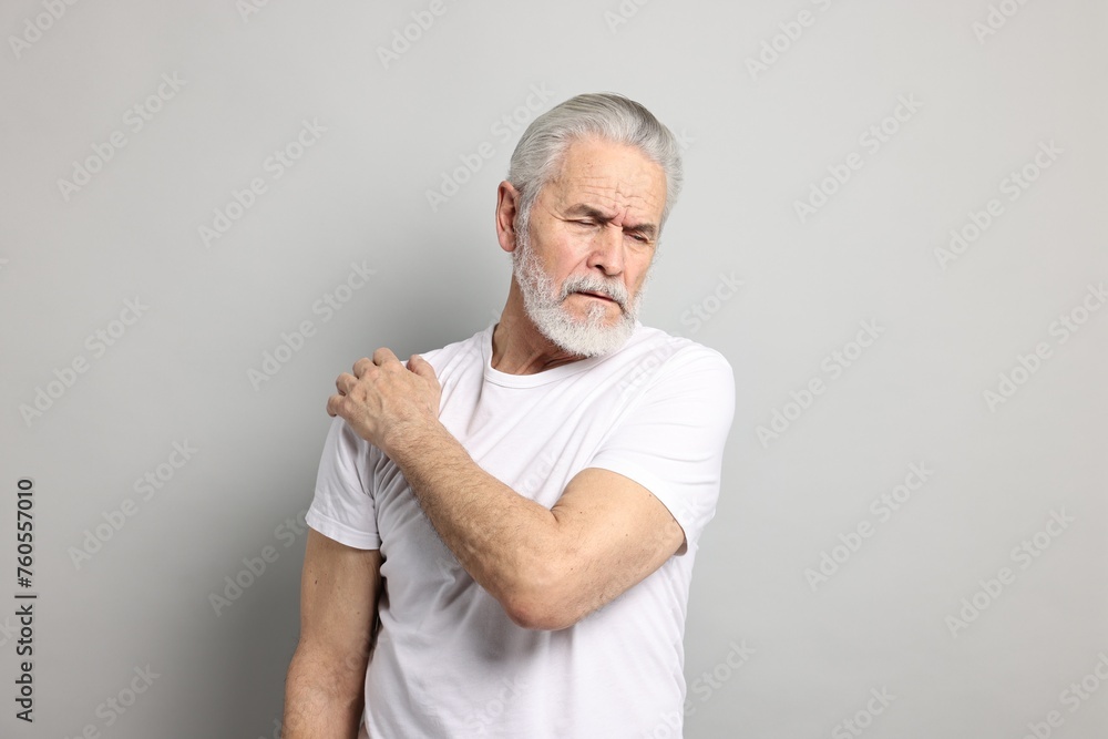 Arthritis symptoms. Man suffering from pain in shoulder on gray background Arthritis symptoms. Man suffering from pain in shoulder on gray background