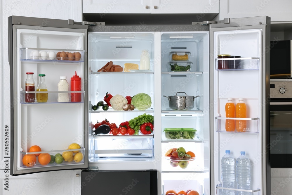 Open refrigerator full of different products in kitchen