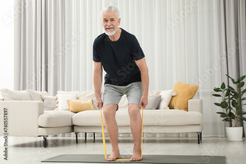 Senior man doing exercise with fitness elastic band on mat at home photo