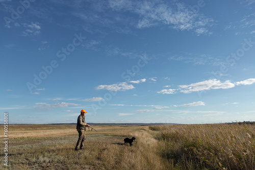 Mature man hunter with gun while walking on field. © Budjak Studio
