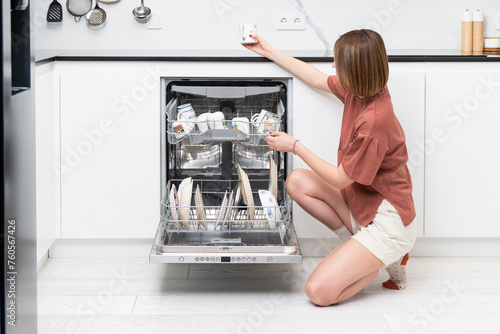 Busy housewife putting dirty plates in dishwasher machine in the kitchen. Household and exhausting cleaning day concept