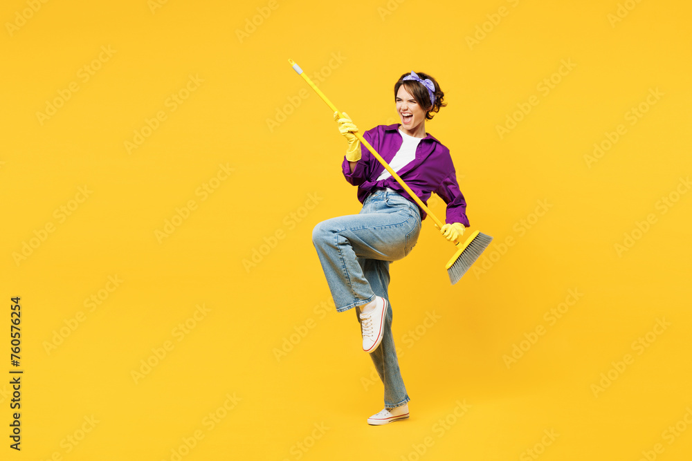 Full body young happy woman wears purple shirt casual clothes do housework tidy up hold in hand brush broom pov play guitar isolated on plain yellow background studio portrait. Housekeeping concept. - obrazy, fototapety, plakaty 