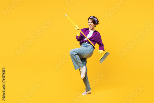 Full body young happy woman wears purple shirt casual clothes do housework tidy up hold in hand brush broom pov play guitar isolated on plain yellow background studio portrait. Housekeeping concept. photo