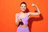 Young fitness trainer sporty woman sportsman wear purple top clothes spend time in home gym show muscles point finger camera on you isolated on plain orange background. Workout sport fit abs concept.