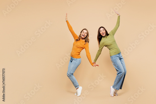 Full body young friends two women wear orange green shirt casual clothes together stand on toes with outstretched hands leaning back dance posing isolated on plain beige background. Lifestyle concept.