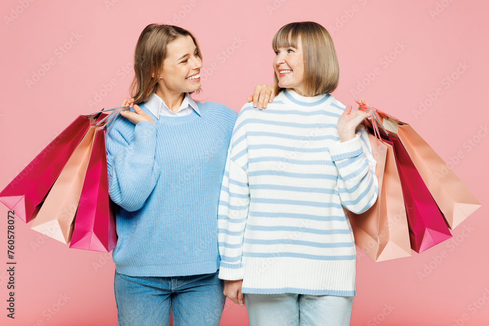 Elder cool parent mom with young adult daughter two women together wear blue casual clothes hold paper package bags after shopping isolated on plain pink background. Black Friday sale buy day concept. Elder cool parent mom with young adult daughter two women together wear blue casual clothes hold paper package bags after shopping isolated on plain pink background. Black Friday sale buy day concept.