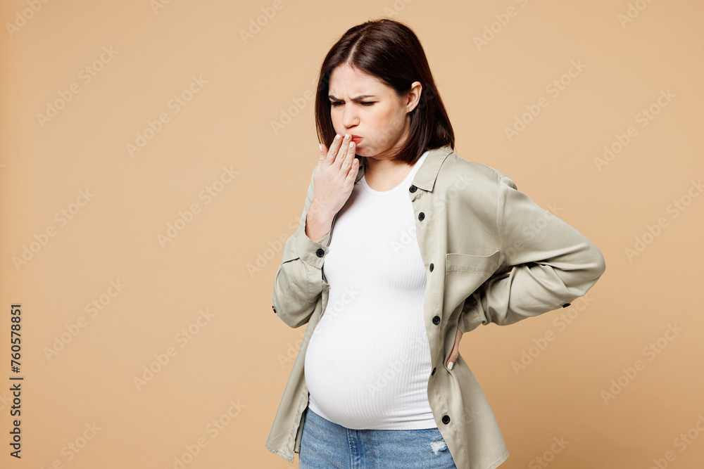 Young sad sick ill pregnant expectant woman future mom wear grey shirt with belly stomach tummy with baby cover mouth with hand isolated on plain beige background. Maternity family pregnancy concept. Young sad sick ill pregnant expectant woman future mom wear grey shirt with belly stomach tummy with baby cover mouth with hand isolated on plain beige background. Maternity family pregnancy concept.