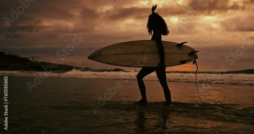 Woman, silhouette and walking with surfboard on beach at night for waves, sport or outdoor surfing in nature. Female person or surfer on ocean coast in late evening for surfing, holiday or weekend photo