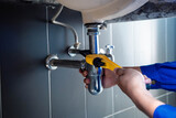 Plumber fixing white sink pipe with adjustable wrench.