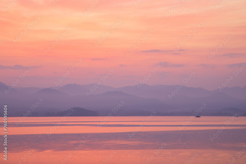 Serene twilight hues reflect off a tranquil lake, with distant mountains shrouded in mist.