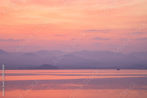 Serene twilight hues reflect off a tranquil lake  with distant mountains shrouded in mist.