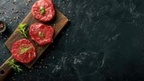 Raw organic marbled beef steaks with spices on a wooden cutting board on a black slate, stone or concrete background. Top view with copy space.