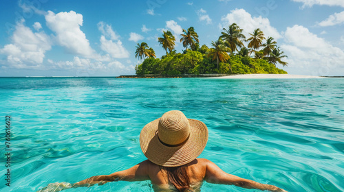 Girl in a chic hat floating in crystal blue waters idyllic island with palm trees and white sands in distance
