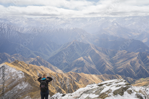 Female hiker standing on top of the mountain enjoying views on mountain ranges in front of her 