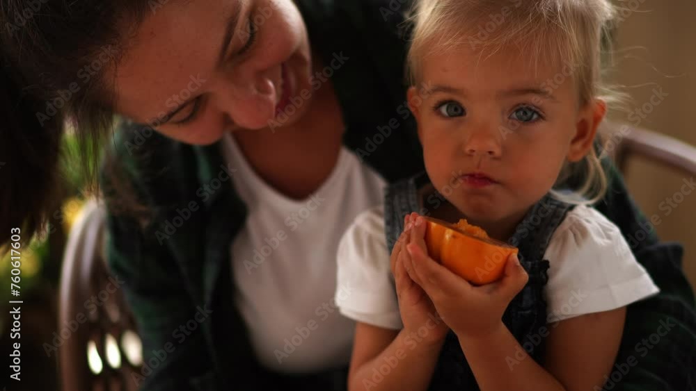 Little girl sits on her mother arms and eats a ripe persimmon. High quality 4k footage Little girl sits on her mother arms and eats a ripe persimmon. High quality 4k footage