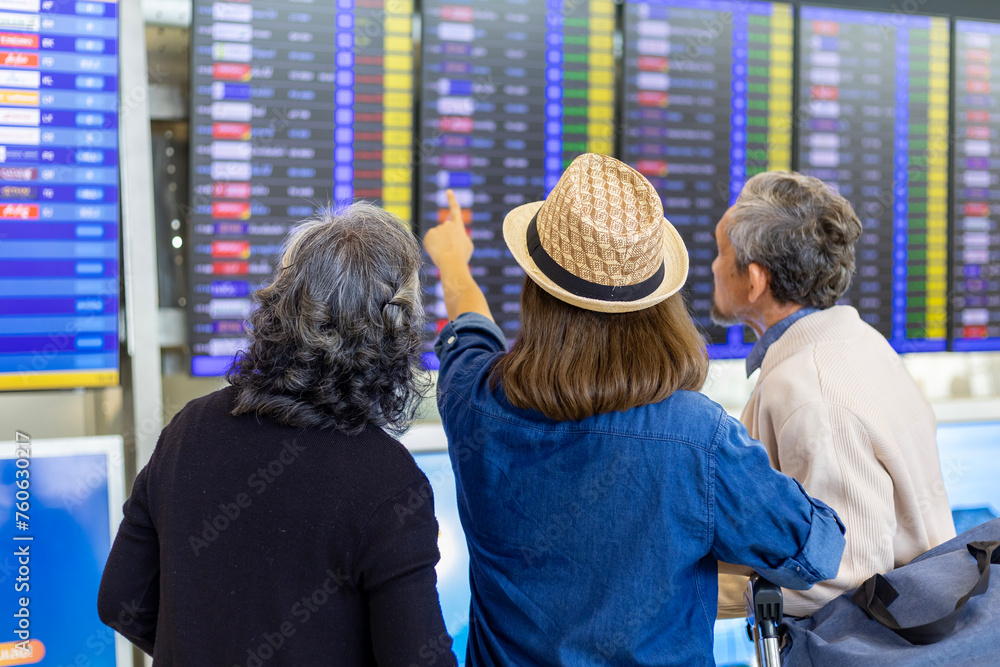 Group of Asian family tourist passenger with senior parent looking at the departure table at airport terminal for airline travel and holiday vacation concept Group of Asian family tourist passenger with senior parent looking at the departure table at airport terminal for airline travel and holiday vacation concept